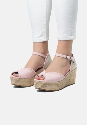 Vaaleanpunaiset kankaiset wedge-sandaalit, joissa on teksturoitu juuttialusta, avonainen varvasdesign ja säädettävä nilkkaremmi. Takana on verkkomateriaali.