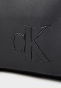 Fekete bőr táska kidomborított "CK" logóval. Textúrált felület sima tapintással, minimalista dizájn, kiegészítő hardver nélkül.