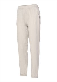 Light beige jogger pants with an elastic waistband, tapered legs, and a soft, textured fabric. Minimalist design with reflective logo detail on side.