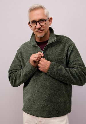 Dark green fleece pullover with a high collar and half zipper. Features a textured surface and long sleeves, worn over a maroon shirt.