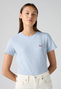 Light blue striped t-shirt with short sleeves, round neckline, and a small red Levi's logo. Paired with high-waisted white jeans.