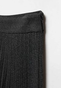 Tela de cuadros gris oscuro en primer plano que muestra la pretina y la cremallera lateral de una prenda confeccionada contra un fondo blanco.