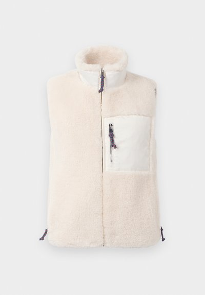 Krém színű, ujjatlan fleece mellény magas gallérral, elülső cipzárral és fehér cipzáras mellzsebbel, amely kék-piros húzózsinórral rendelkezik.