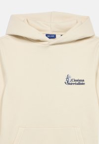 Μπεζ φούτερ με κουκούλα και κορδόνι, με ένα μικρό μπλε και μαύρο γραφικό "Cinéma Surréaliste" στο στήθος και τσέπη καγκουρό.