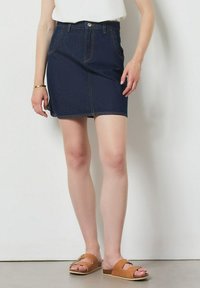 Džínová sukně v tmavě modré barvě, do poloviny stehna, s předními kapsami a mírně tvarovaným A-linem. V kombinaci s hnědými nazouváky.