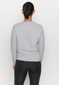 Felpa grigia con maniche lunghe, design raglan, colletto rotondo e polsini a costine. Indossata con leggings neri, vista dal retro.
