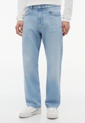 Φωτεινά γαλάζια τζιν με ίσιο πόδι, φορεμένα με λευκά αθλητικά παπούτσια και λευκό μακρυμάνικο πουκάμισο, μπροστινή όψη από τη μέση μέχρι τα πόδια.