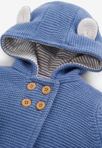 Zila adīta jaka ar kapuci un lāča ausīm. Iekšējā oderē ir svītras, koka pogas un teksturēta virsma.