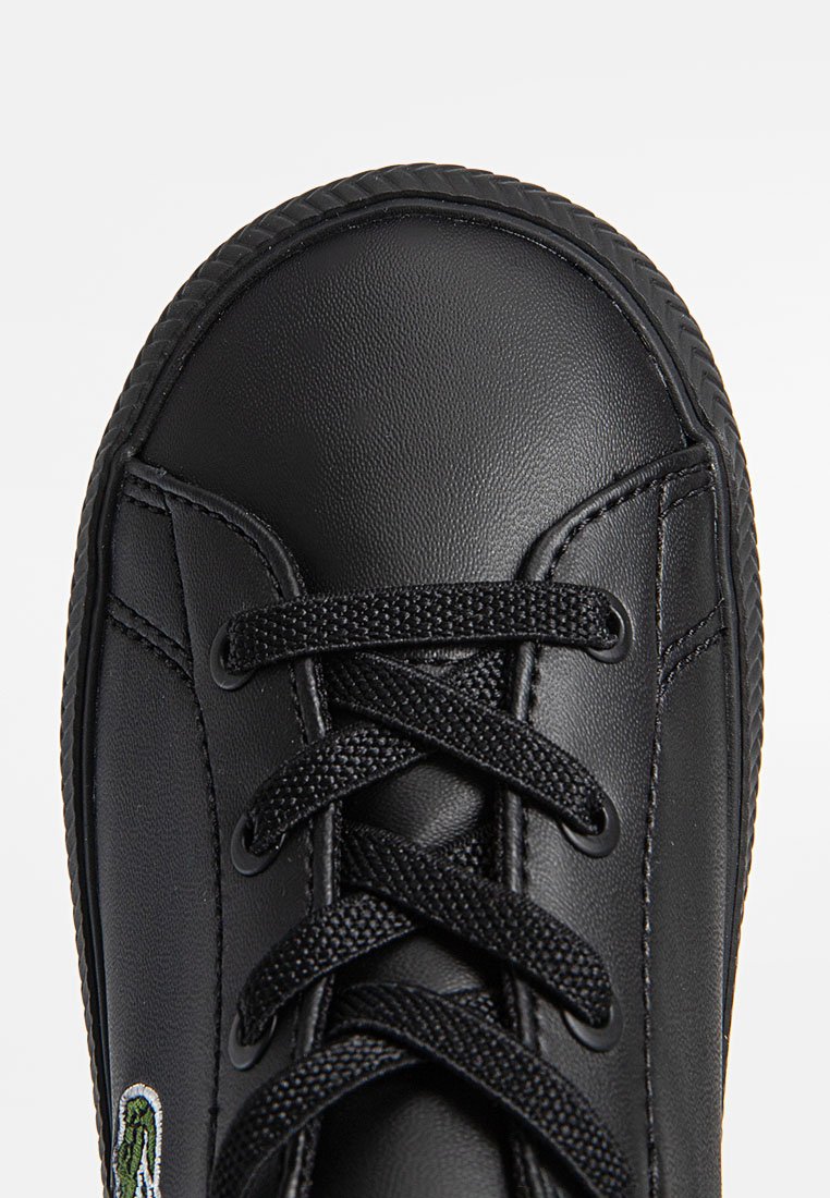 Czarne syntetyczne sneakersy z zaokrąglonym noskiem, teksturowaną cholewką i czarnymi sznurowadłami. Na boku znajduje się zielone haftowane logo.