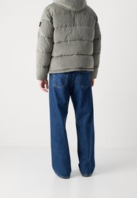 Szara kurtka puchowa ze sztruksu z kapturem, połączona z szerokimi niebieskimi dżinsami o szerokich nogawkach. Kurtka posiada poziome pikowane sekcje oraz subtelne oznaczenia marki.