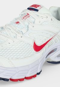 Λευκό αθλητικό παπούτσι Nike Air Max με κόκκινο λογότυπο Swoosh και κόκκινες και ναυτικές λεπτομέρειες στη σόλα και τη γλώσσα, με υφή από διχτυωτό ύφασμα και κορδόνια.
