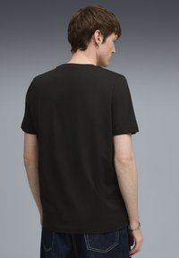 Camiseta negra de manga corta con cuello redondo, textura suave y corte regular, vista desde atrás. Diseño minimalista, sin patrones.