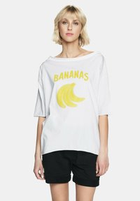Biała, oversize'owa koszulka z napisem "BANANAS" na żółto, umieszczonym nad grafiką banana. Wykonana z miękkiej bawełny, z szerokim dekoltem i krótkimi rękawami.