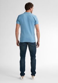 Světle modré texturované polo tričko s límečkem, spárované s tmavými džíny a bílými teniskami, zobrazené ze zadu.