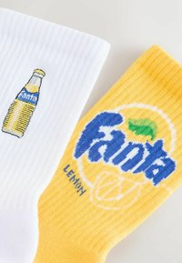 White sock with yellow Fanta bottle embroidery; yellow sock with blue "Fanta" logo and lemon graphic. Both have ribbed texture.