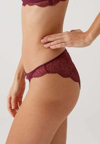 Bordeaux kantondergoed met geschulpte randen, versierd met bloemenpatronen en een lichte afwerking. De textuur lijkt delicaat en enigszins transparant.