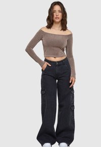 Bruine off-the-shoulder top met lange mouwen en een aansluitende pasvorm; gecombineerd met hoge zwarte cargobroek met zijzakken.