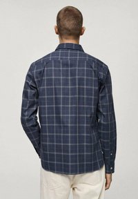 Donkerblauw geruit overhemd met een gestructureerde kraag, lange mouwen en knoopmanchetten. Heeft een geruit patroon in wit en lichtblauw.