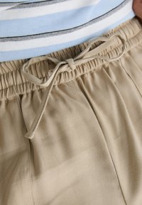 Beige shorts med resårmidja och dragsko. Tyget har en texturerad yta med veck framtill.