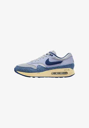 Zapatilla deportiva azul y gris con una superposición de malla azul texturizada, paneles lisos en gris claro y una amortiguación de aire visible en la suela.