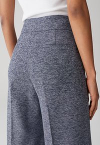 Pantalons larges en tissu bleu texturé, dotés d'une taille haute et de deux poches arrière. Le motif est un léger chevron.