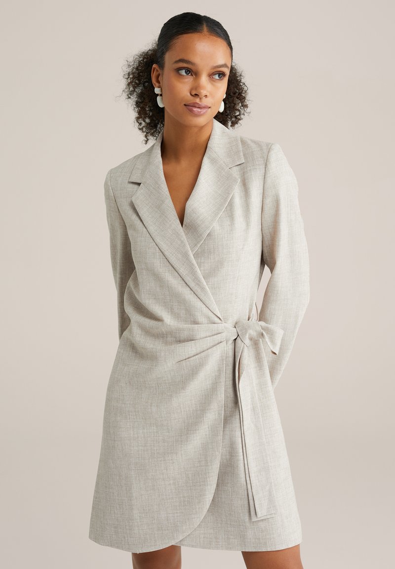 Vestito avvolgente grigio chiaro con tessuto strutturato, caratterizzato da colletto con intaccatura e vita annodata. Maniche lunghe e lunghezza al ginocchio.