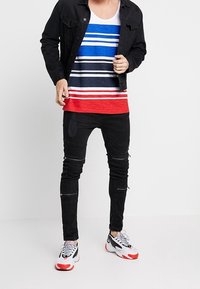 Svart denimjacka, blå och vit randig linne med röda detaljer, slitna svarta jeans och färgglada träningsskor.