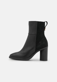 Bottine noire avec une combinaison de cuir lisse et de daim. Elle présente un talon bloc, un bout arrondi et une languette à l'arrière.
