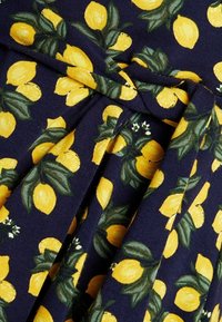 Marinfärgad tyg med ett mönster av citroner och blad, som har livliga gula citroner och gröna blad. Texturerad, med detaljer vid midjan som knyts.