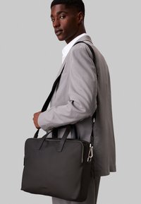 Maletín negro con dos asas superiores y una correa de hombro desmontable. Material suave, forma rectangular y detalle de cremallera plateada.