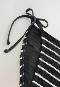 Bikini zgornji del v črno-belem črtastem vzorcu iz teksturiranega materiala, ki ima zavezo in gladko črno podlogo. Poudarki vključujejo nabranje.
