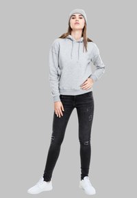 Haut à capuche gris avec cordons et poignets côtelés, associé à un jean skinny noir usé et des baskets blanches. Le modèle porte également un bonnet gris.