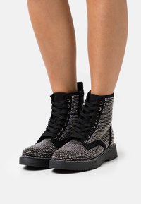Black ankle boots featuring rhinestone embellishments, black laces, a rugged sole, and a layered design with a suede finish.