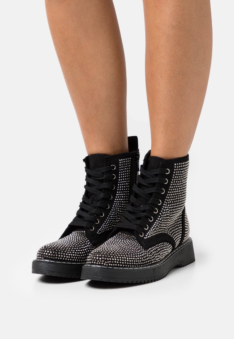 Black ankle boots featuring rhinestone embellishments, black laces, a rugged sole, and a layered design with a suede finish.