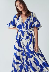 Sininen ja valkoinen kukkakuosiset mekko, jossa on V-pääntie, lyhyet hihat, vyötärönauha ja kerroksellinen hame, mikä luo valuvaa muotoilua. Puuvillamateriaali.