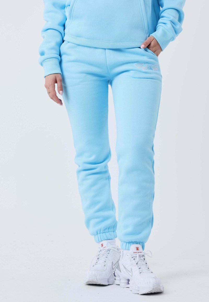 Lyseblå træningsbukser i et blødt stof med elastiske manchetter. Har et lille logo på hoften og sidelommer.