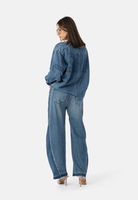 Denimjakke og vidbeinte jeans i lyseblått. Jakken har logo bak og relaxed passform. Strukturert stoff med frynsete mansjetter. Sko med hæl.