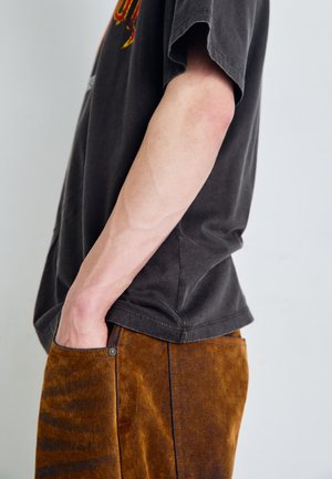 Black cotton t-shirt with a relaxed fit and short sleeves, paired with brown corduroy pants featuring a pocket with a metallic button detail.