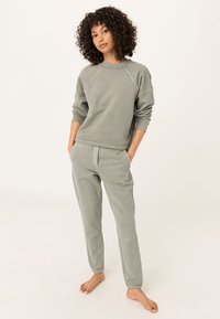 Sudadera gris claro y pantalones de chándal a juego hechos de una tela suave y texturizada. Cuenta con mangas raglán y bolsillos en los pantalones.
