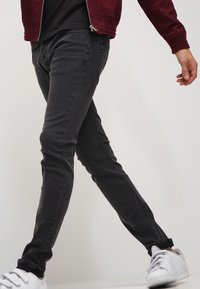 Jeans de mezclilla negros ajustados con un ligero estiramiento, que presentan un diseño clásico de cinco bolsillos. Combinados con zapatillas blancas para un contraste.