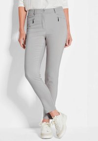 Lichtgrijze slim fit broek met twee voorzakken met rits, een gladde textuur en een hoge tailleband, gedragen met witte sneakers.