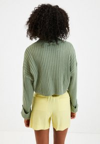 Maglione verde a coste con colletto abbinato a pantaloni corti gialli con orlo scallop. Il tessuto sembra testurizzato e leggero.
