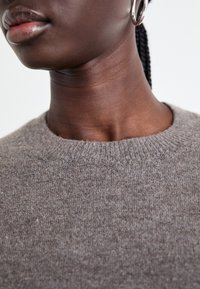 Pull en tricot gris avec un col rond et un tissu texturé, montrant un gros plan des matériaux et du teint, mettant en valeur le contraste visuel.