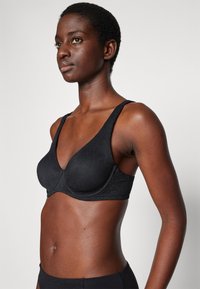 Zwarte beha met een diepe V-hals en verstelbare brede schouderbanden. Gemaakt van textiel met een gladde afwerking. Sluit nauw aan op het lichaam.