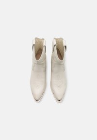Botas de tobillo blancas de cuero con puntera afilada, costuras decorativas y acentos metálicos en la suela. Textura suave, diseño minimalista.