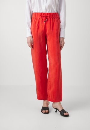 Pantaloni larghi leggeri rossi con vita regolabile e tessuto texturizzato, abbinati a tacchi aperti neri.