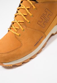 Bruine leren laars met oranje veters, gestructureerde bovenkant, rubberen zool en reliëflogo. Heeft metalen oogjes en versterkte stiksels.