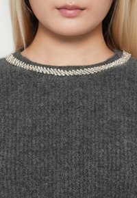 Pull gris en tissu texturé à côtes. Rehaussé d'une embellissement scintillant en argent tissé autour de l'encolure.