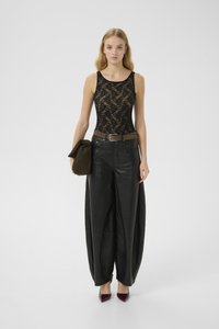 Woman stands wearing black lace sleeveless top and wide black leather pants, holding olive green clutch, paired with maroon pointed heels.