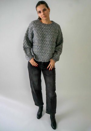Pull en maille grise avec un motif texturé, jeans noirs et bottines noires. Le pull a une coupe décontractée et des poignets côtelés.